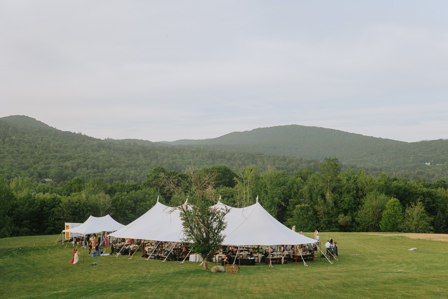 Guests gather under white Sperry tents for a colorful mountaintop wedding reception in Stowe, Vermont.