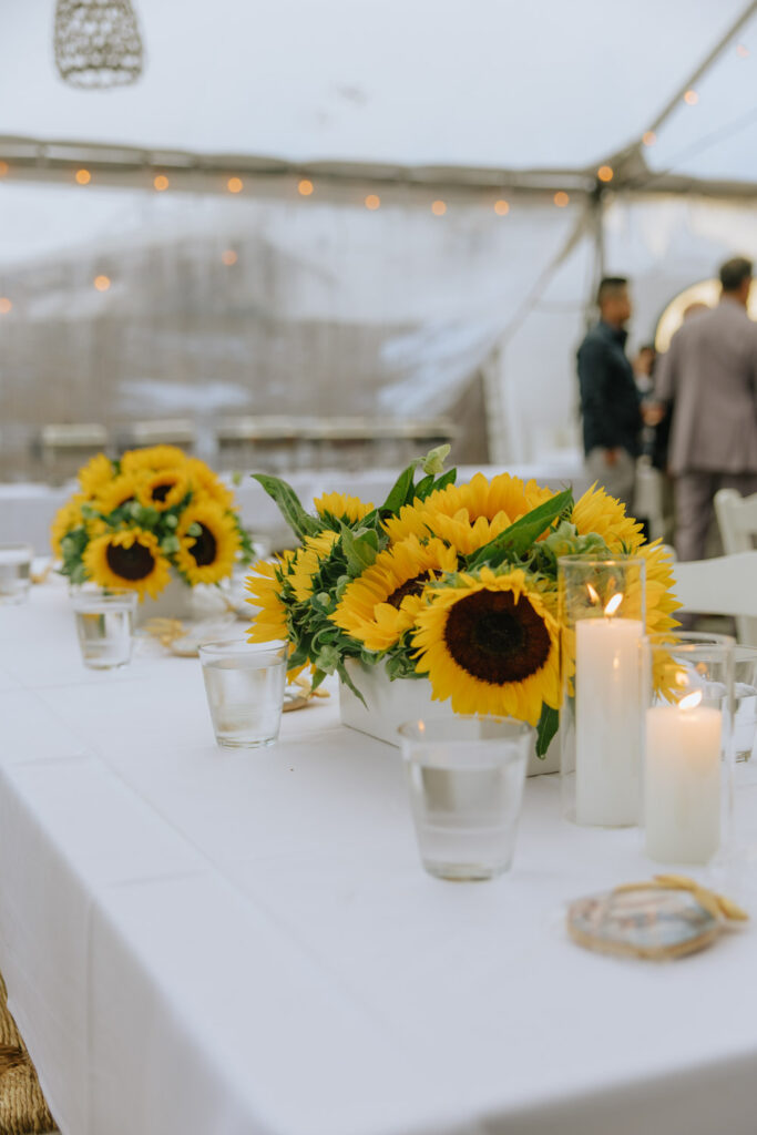 A close-up of sunflower centerpieces and lit candles on a white-clothed table at a Hamptons wedding.