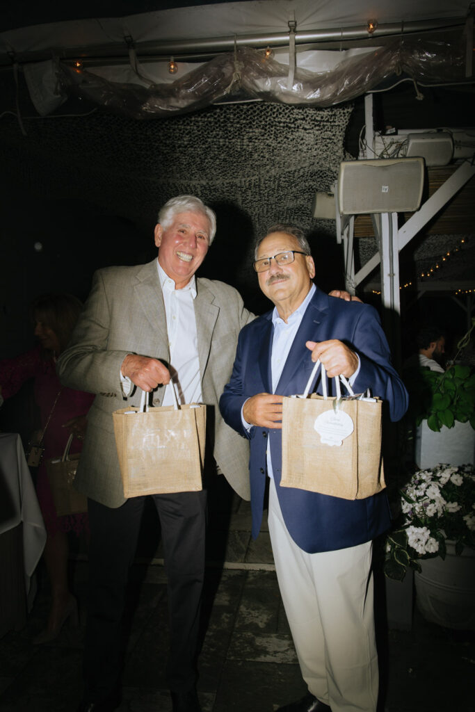 Two men hold gift bags at a Bridgehampton Tennis & Surf Club wedding reception in New York.