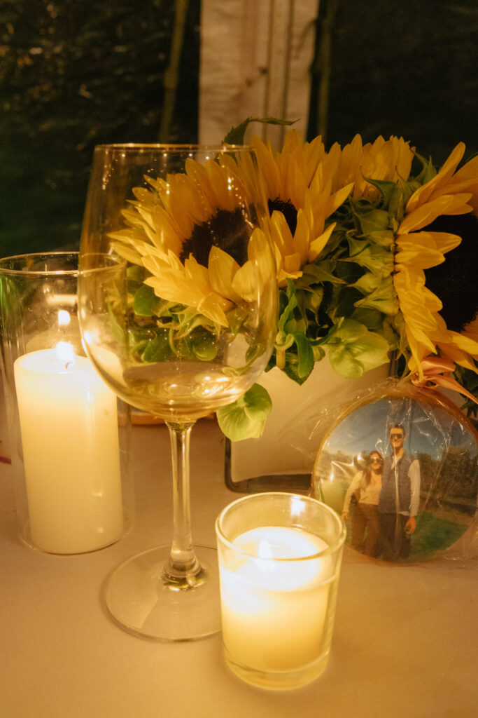 Decorative sunflowers, candles, wine glass, and a personalized cookie on a table at a wedding.