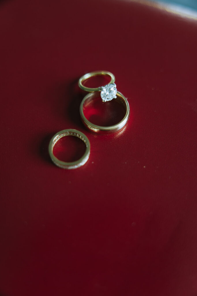Three gold wedding rings with a large diamond on a red surface at a Bridgehampton wedding.
