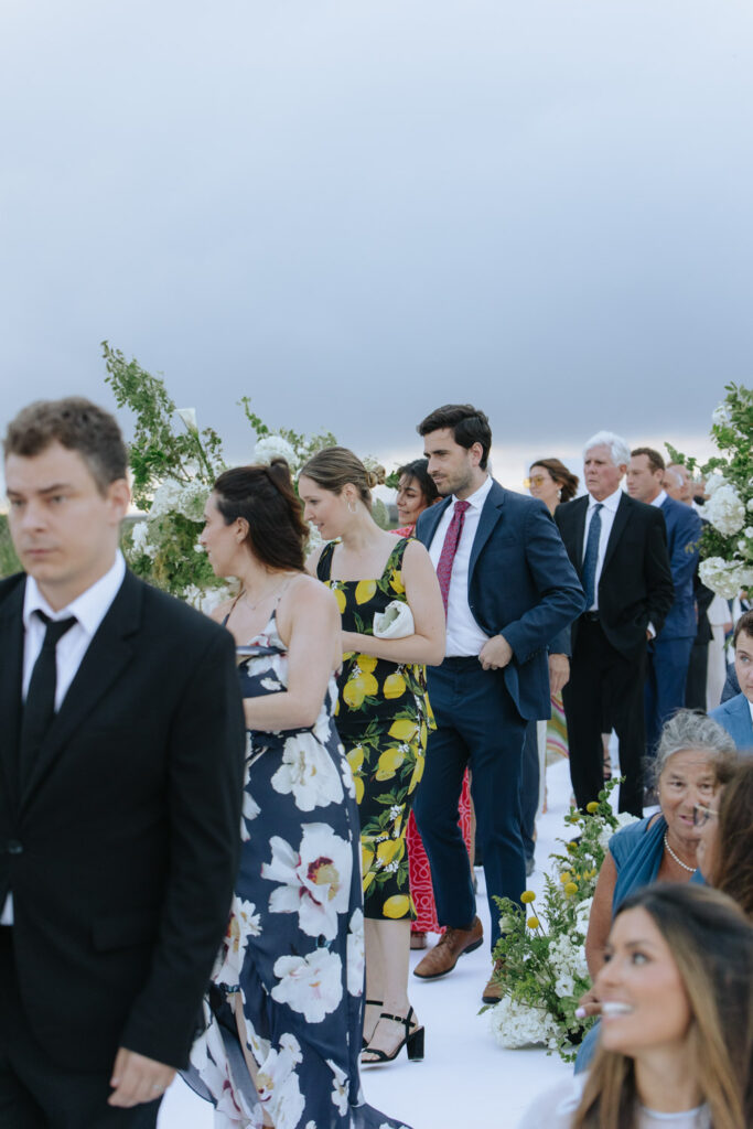 Guests walk down an aisle lined with white flowers at a Bridgehampton Tennis & Surf Club wedding.