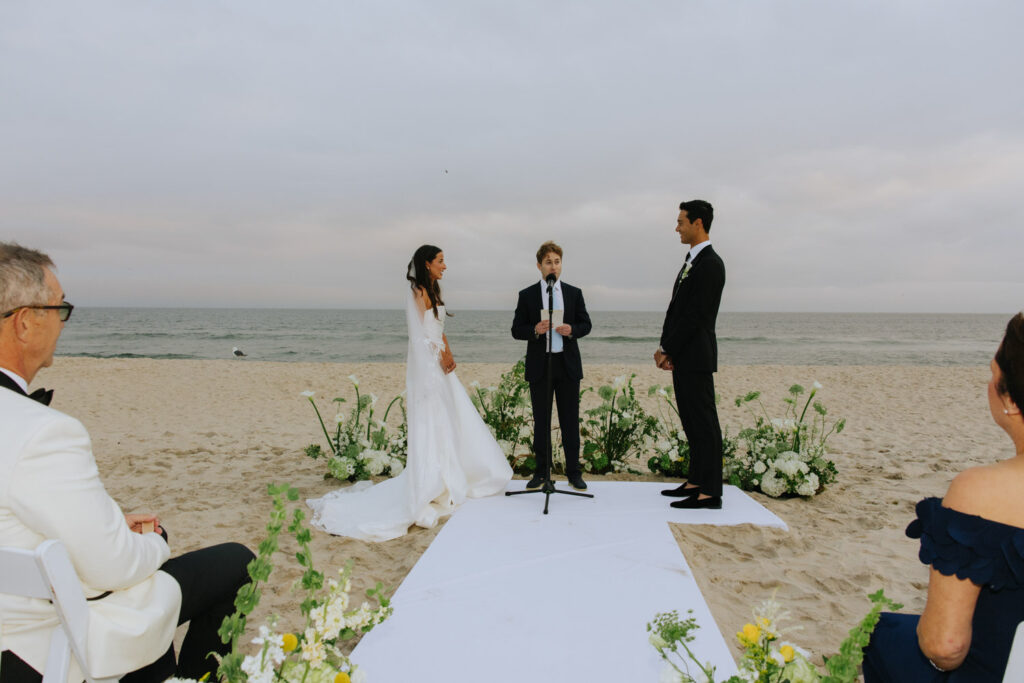 A couple exchanges vows on a white runner on the sand during their Bridgehampton Tennis & Surf Club wedding.