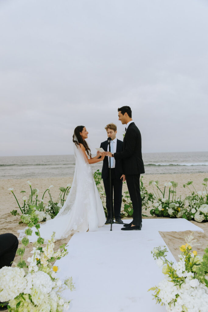 Bride and groom exchanging vows on the sand with officiant at their Bridgehampton Tennis & Surf Club wedding.