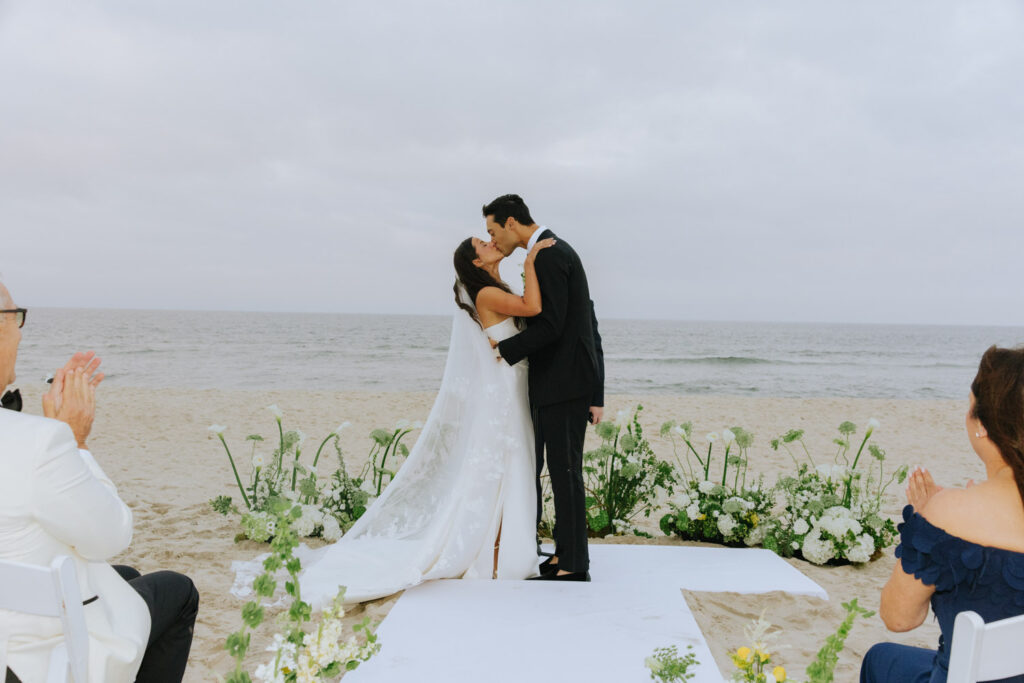 A bride and groom kiss on the sandy beach during their Bridgehampton Tennis & Surf Club wedding.