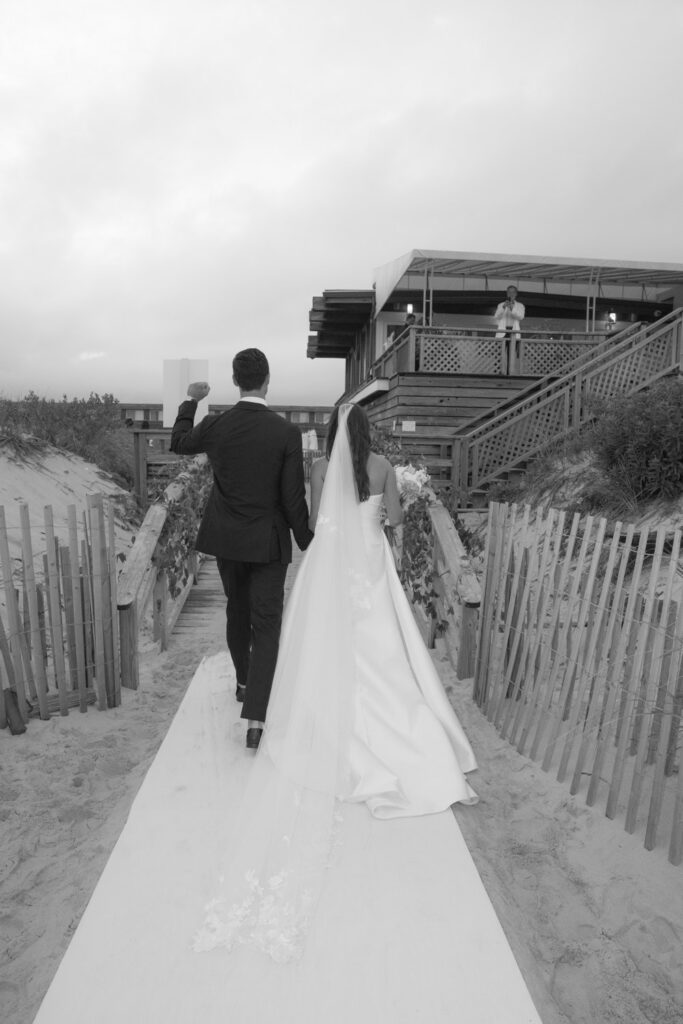 Groom and bride walk up a ramp to the Bridgehampton Tennis & Surf Club wedding venue.