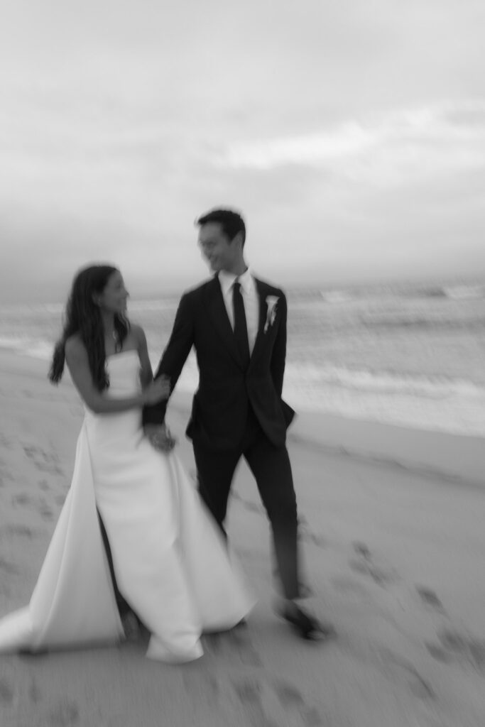 A newlywed couple walking hand-in-hand on the beach during their Bridgehampton Tennis & Surf Club wedding.