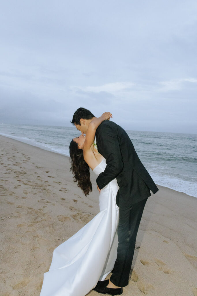 Groom dips bride for a kiss on the sandy beach at Bridgehampton Tennis & Surf Club wedding.