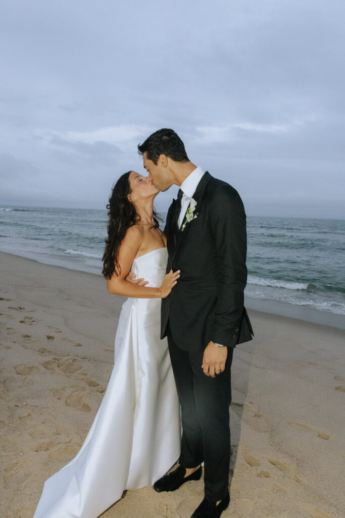 Newlyweds kiss on the sandy beach of their Bridgehampton Tennis & Surf Club wedding in New York.