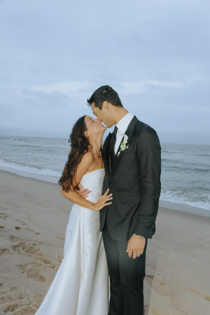 A bride and groom share a kiss on the sandy beach at their Bridgehampton Tennis & Surf Club wedding.