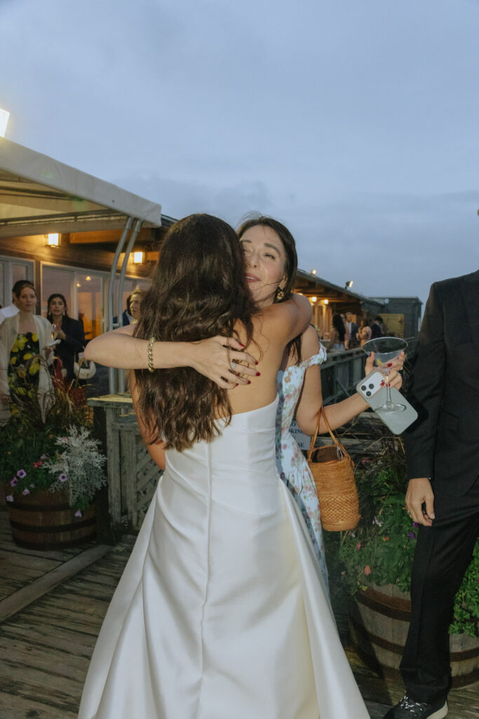 A woman in a white wedding gown embraces a guest at a Bridgehampton Tennis & Surf Club wedding.