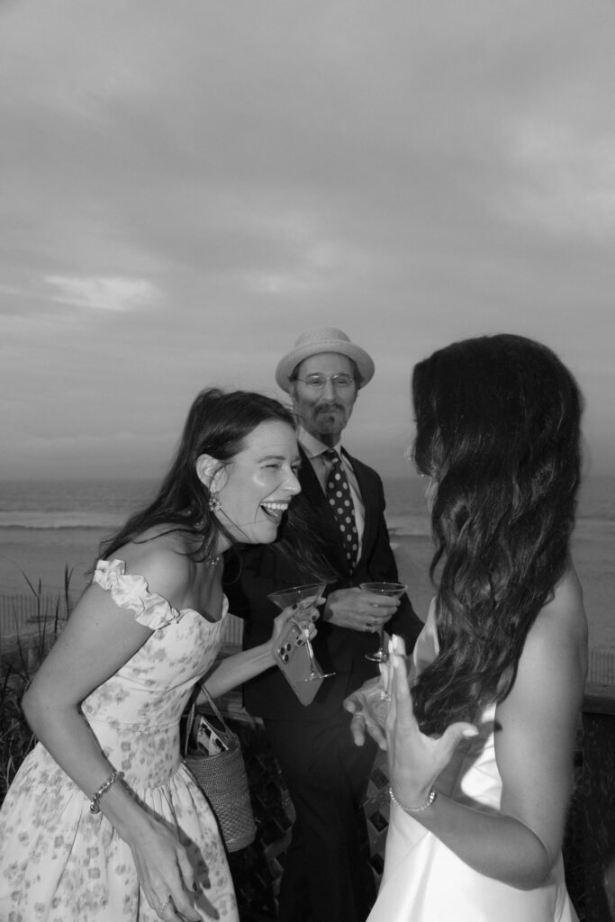 Wedding guests laughing and holding drinks on a deck overlooking the Atlantic Ocean in Bridgehampton.