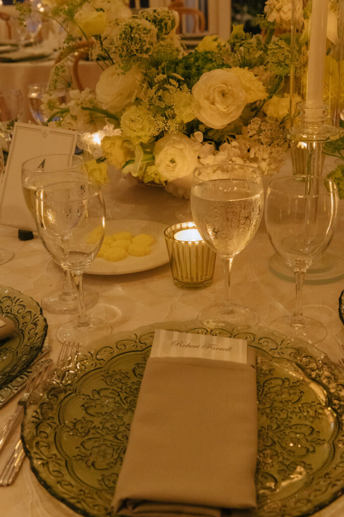 A formal place setting with green glass plates, a name card, and a floral centerpiece at a wedding.