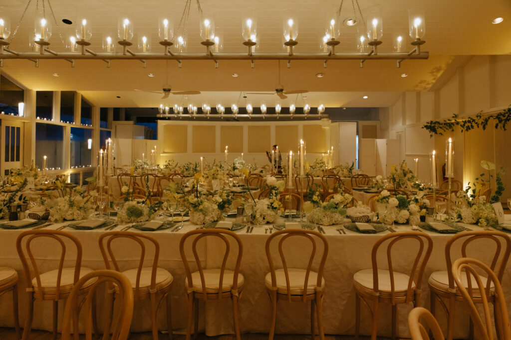 Long reception tables with floral arrangements, candles, and place settings at Bridgehampton Tennis & Surf Club.