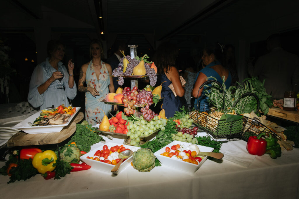 Guests gather around a wedding buffet of fresh fruit, vegetables, and small bites at Bridgehampton Tennis & Surf Club.