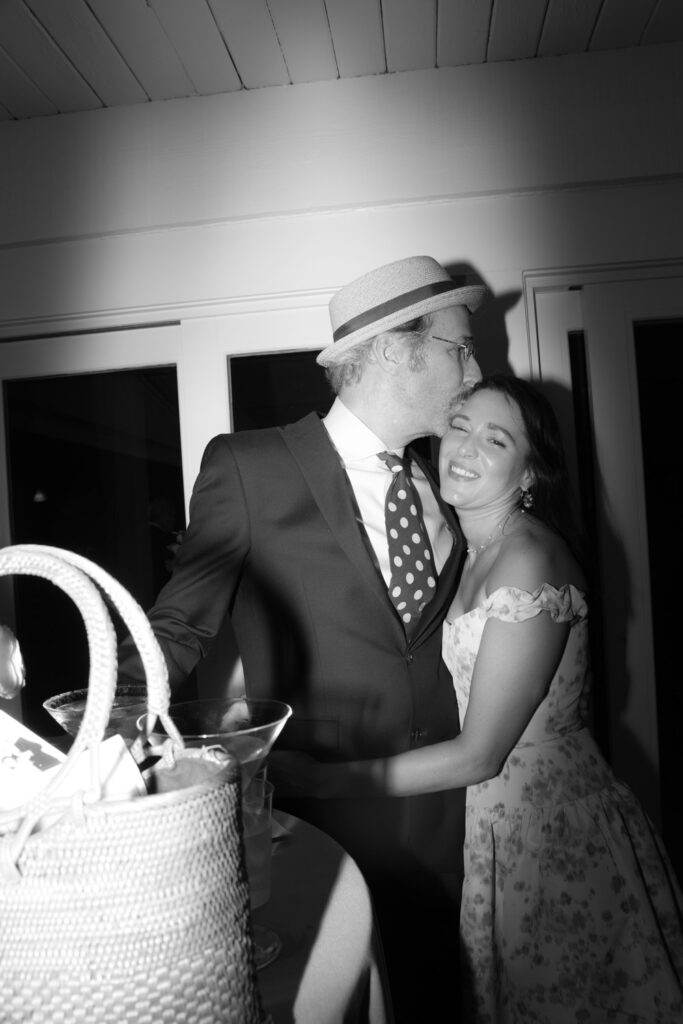 A man in a hat kisses a woman's forehead during a Bridgehampton Tennis & Surf Club wedding.