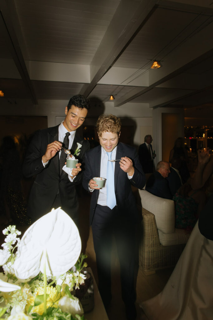 Two men smile while eating dessert at a Bridgehampton Tennis & Surf Club wedding reception.