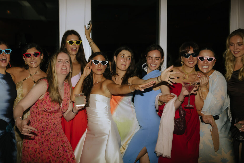 Group of women in dresses and sunglasses pose and laugh at a Bridgehampton Tennis & Surf Club wedding.