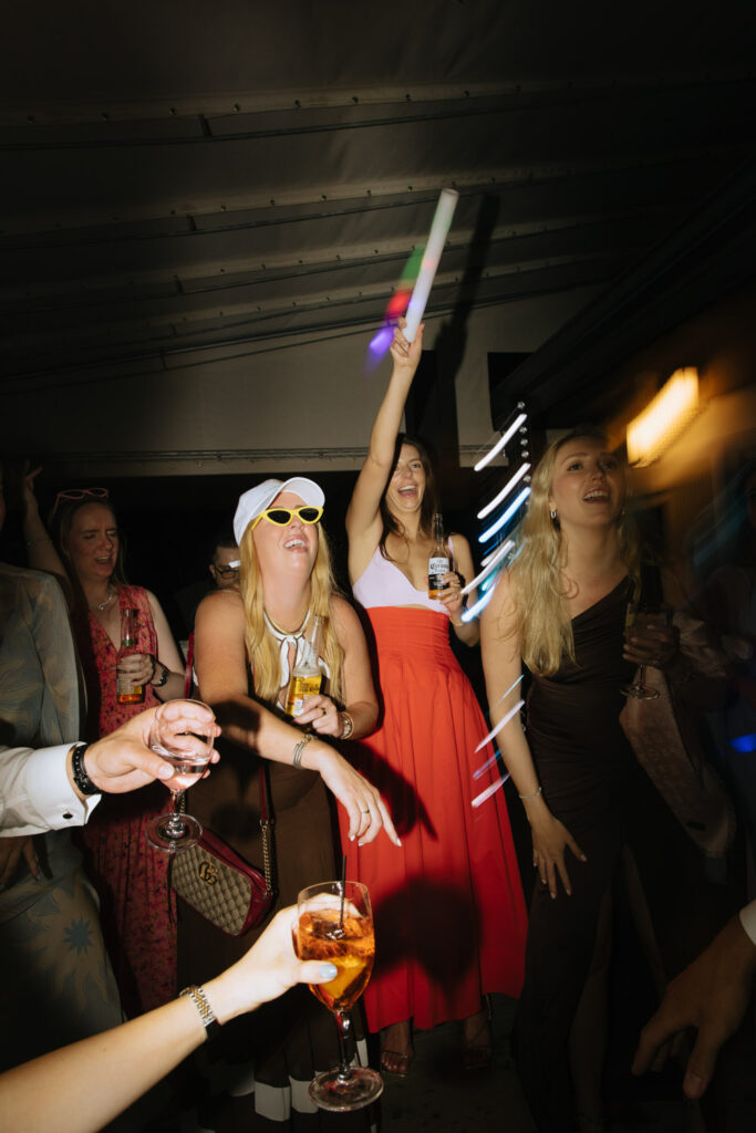 Wedding guests dance with drinks and a glow stick at a Bridgehampton Tennis & Surf Club wedding.