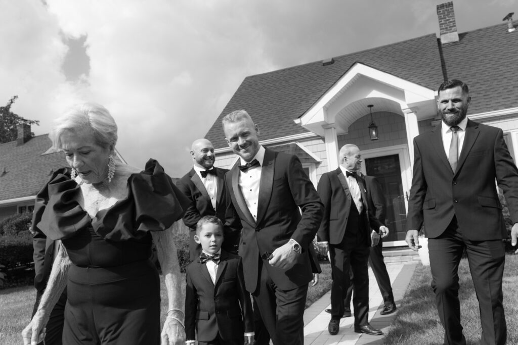 An older woman, men, and a boy in formal wear walk outside a residence for a Russos on the Bay wedding.