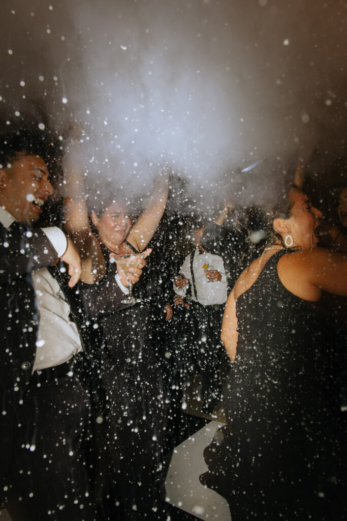 Wedding guests dancing under falling particles and smoke at a Russos on the Bay wedding reception.