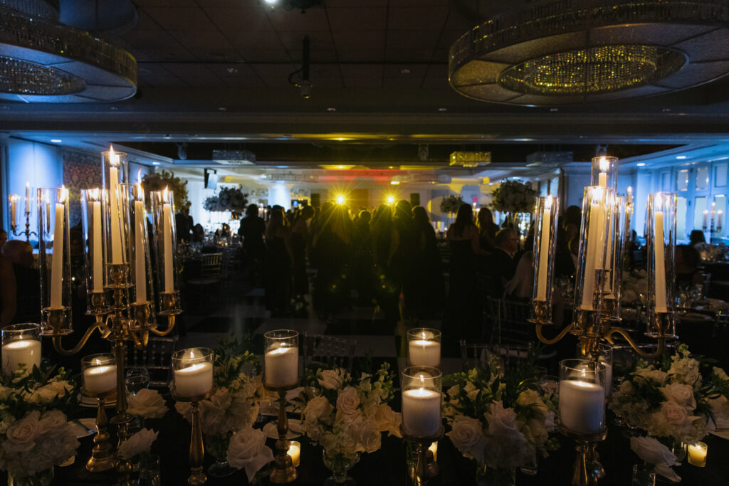 Wedding guests on a dance floor with a table in the foreground decorated with candles and flowers at Russos on the Bay.