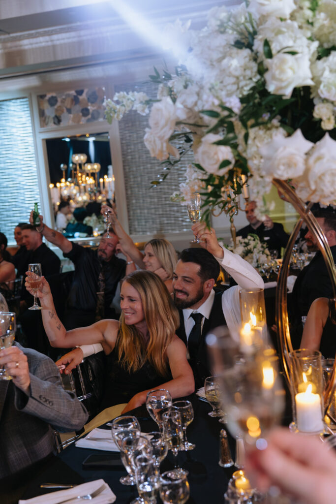 Wedding guests raise champagne glasses for a toast at a wedding reception at Russo's On The Bay.