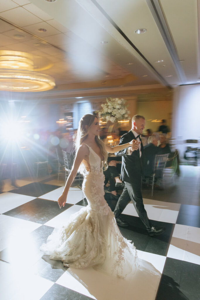 Newlyweds walk across a checkered dance floor at their Russos on the Bay wedding reception.