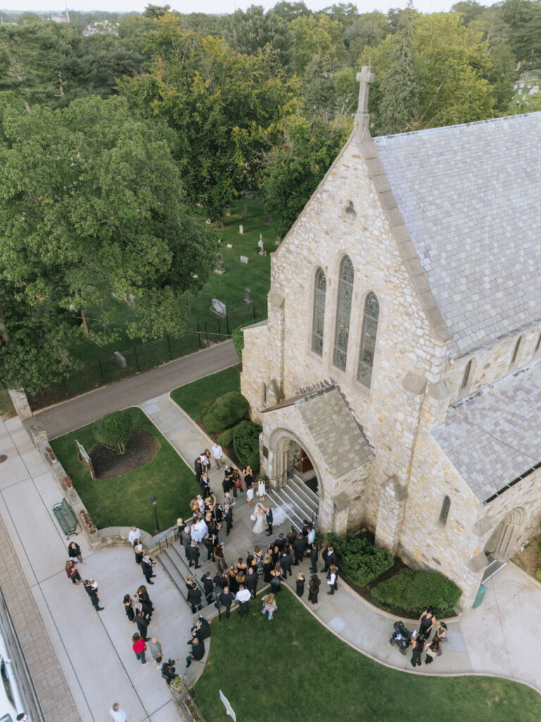 Aerial view of wedding guests gathered outside the church after a Catholic ceremony at Russos on the Bay.