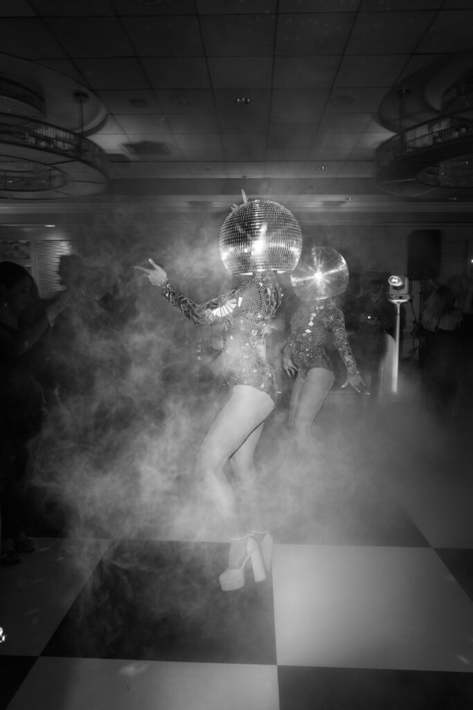 Dancers in disco ball costumes performing in smoke on a checkered dance floor at a Russos on the Bay wedding.