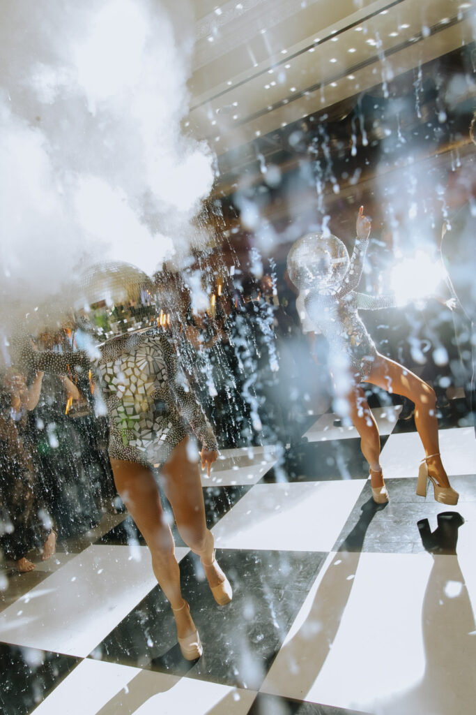 Dancers in disco ball outfits perform on a black and white checkered floor at a Russos on the Bay wedding.