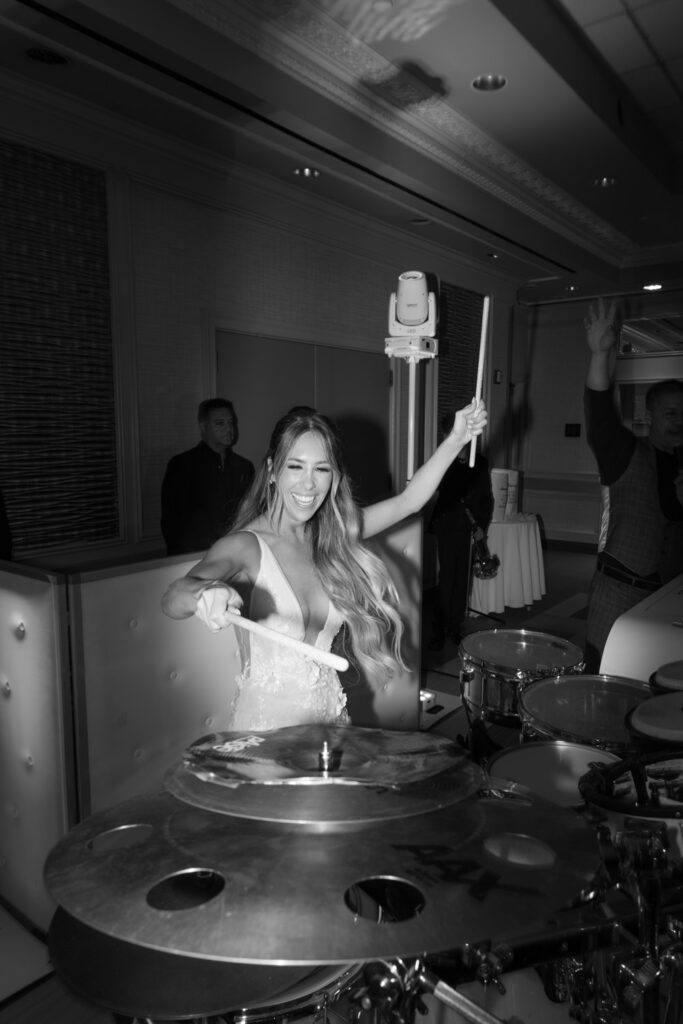 A bride plays drums with drumsticks at her wedding reception at Russos on the Bay.