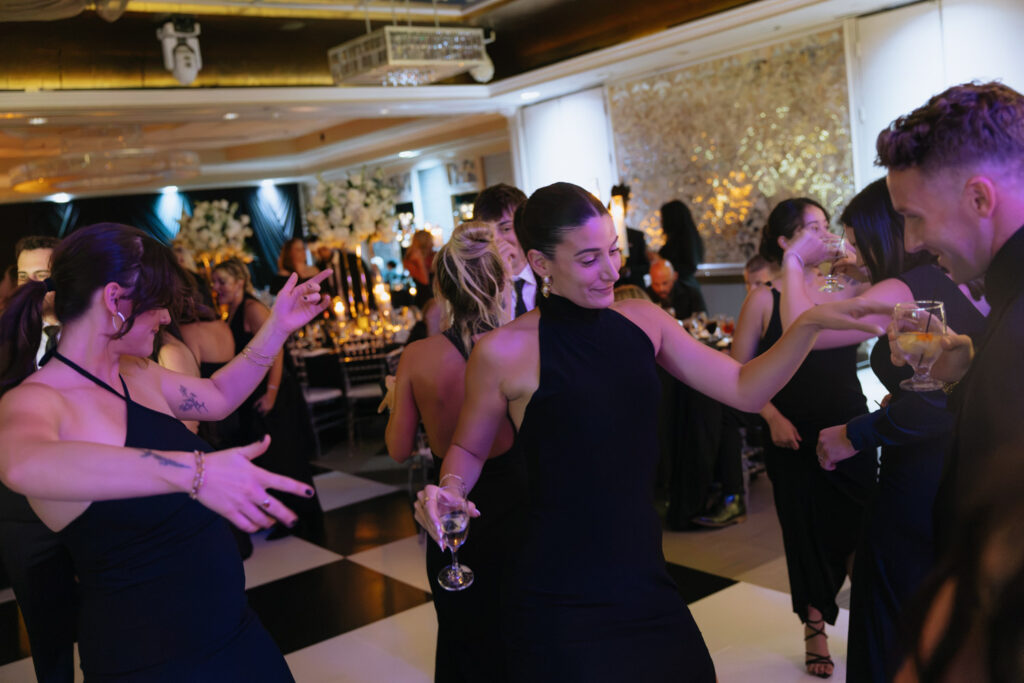 Guests in formal attire dance on a black and white checkered floor at a wedding reception at Russo's On The Bay.