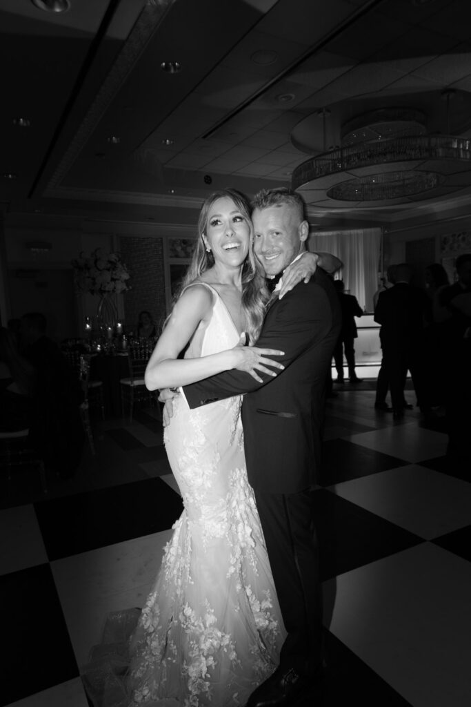 A newlywed couple embraces on a black and white checkered dance floor at their Russos on the Bay wedding.