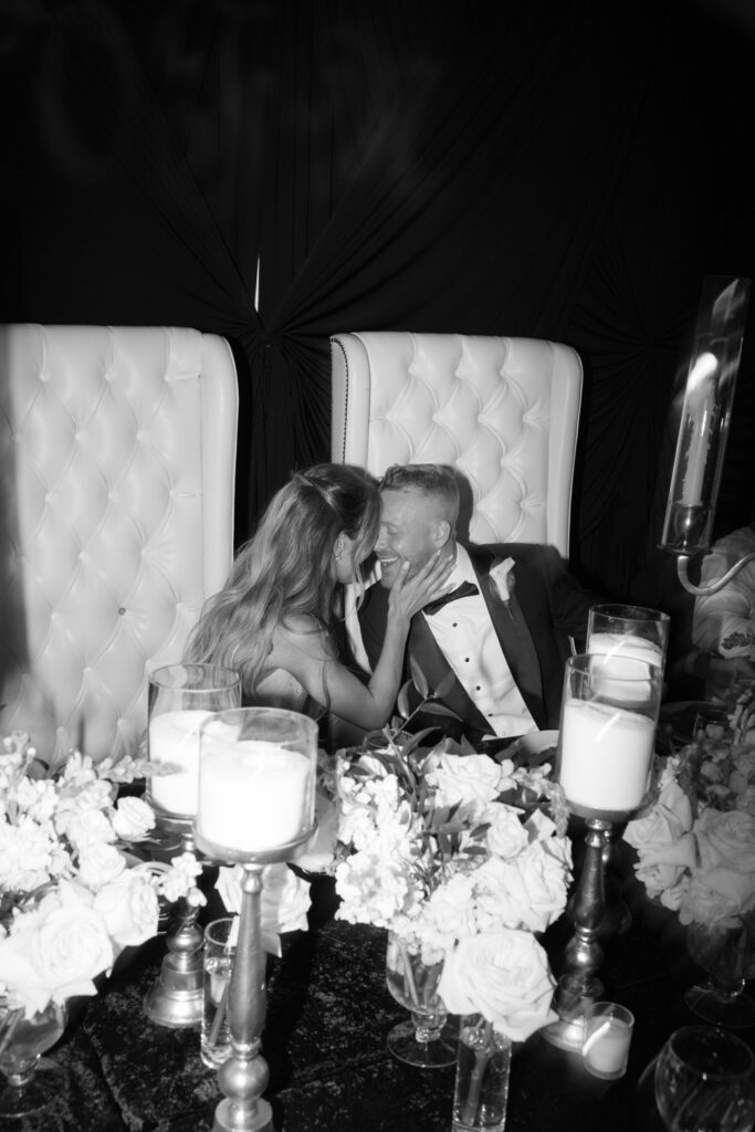 A newlywed couple laughing and embracing at their table during a Russos on the Bay wedding reception.