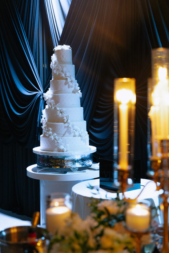 A multi-tiered white wedding cake with white floral accents at a wedding at Russos on the Bay.