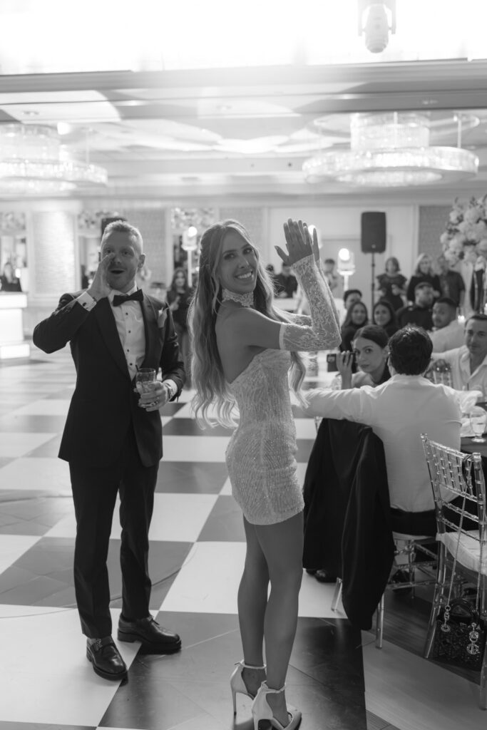 A man cheering and a woman clapping on a checkered dance floor at a wedding at Russo's On The Bay.