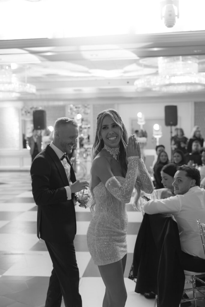 A bride in a short wedding dress and a groom smile while guests celebrate at Russo's On The Bay.