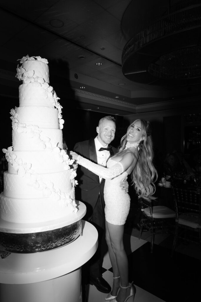 documentary wedding photographer captures A newlywed couple posing with a towering multi-tiered wedding cake at Russos on the Bay.