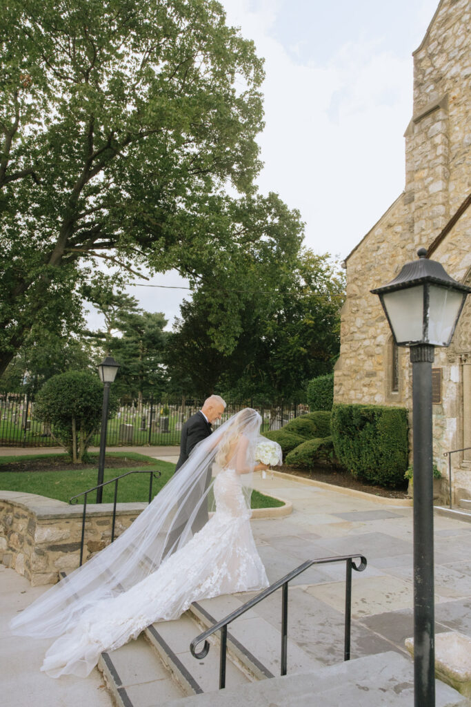 A bride with a long veil walks down steps with a man at her Catholic church wedding ceremony.