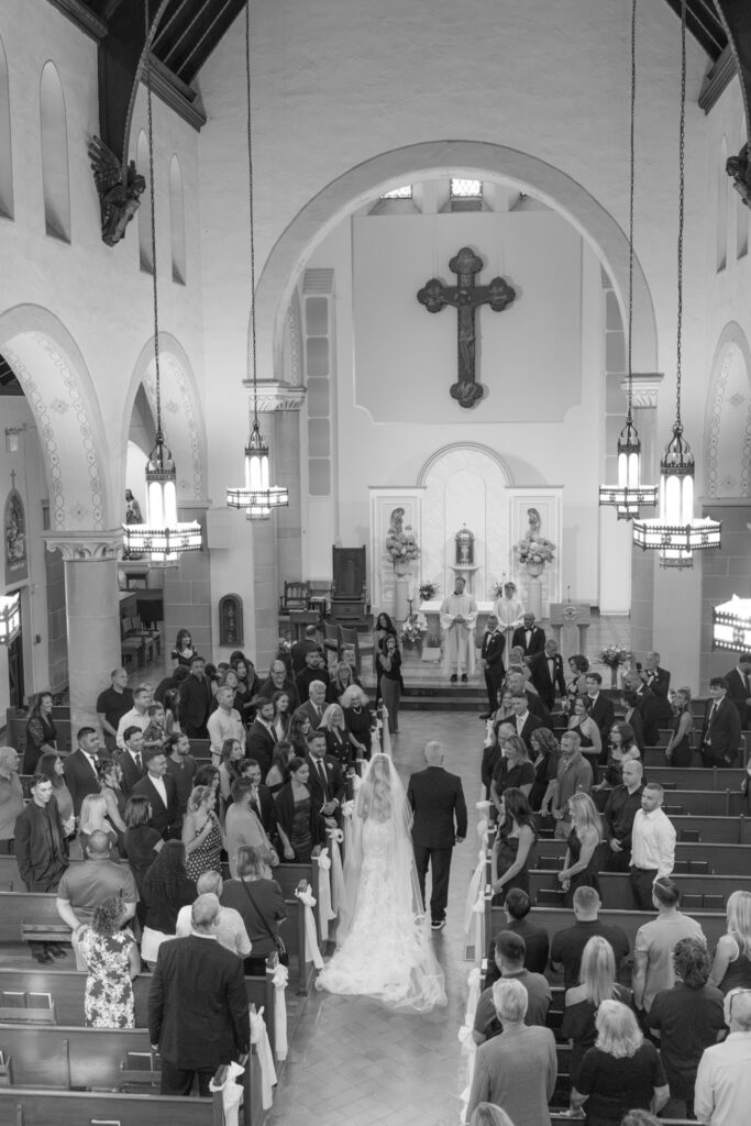A bride and father walk down the aisle towards the altar in a Catholic church wedding.