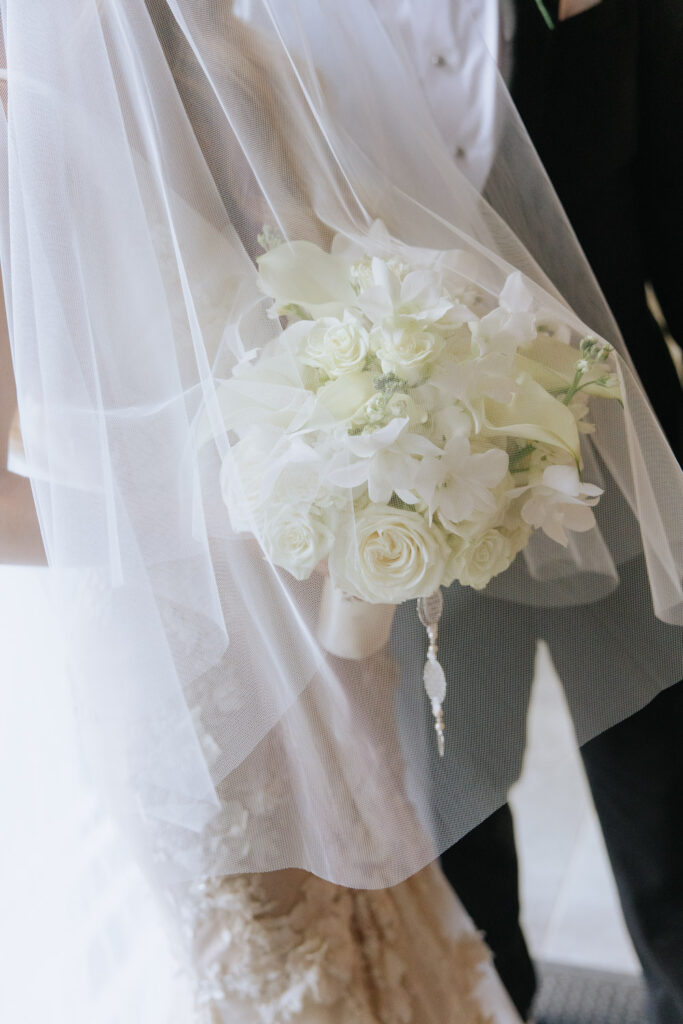A bridal bouquet with white roses and orchids under a veil at a wedding at Russos on the Bay.