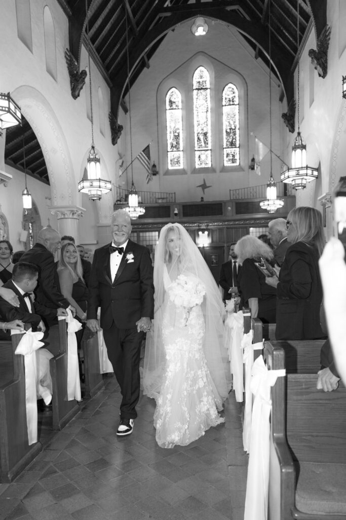 A man and a bride walk hand-in-hand down the aisle of a Catholic ceremony at Russo's On The Bay.