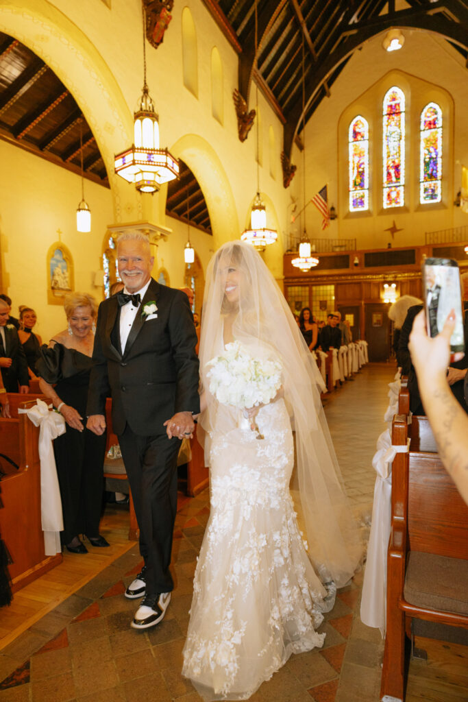 Father and bride walk down the aisle during a Catholic ceremony at Russos on the Bay wedding.