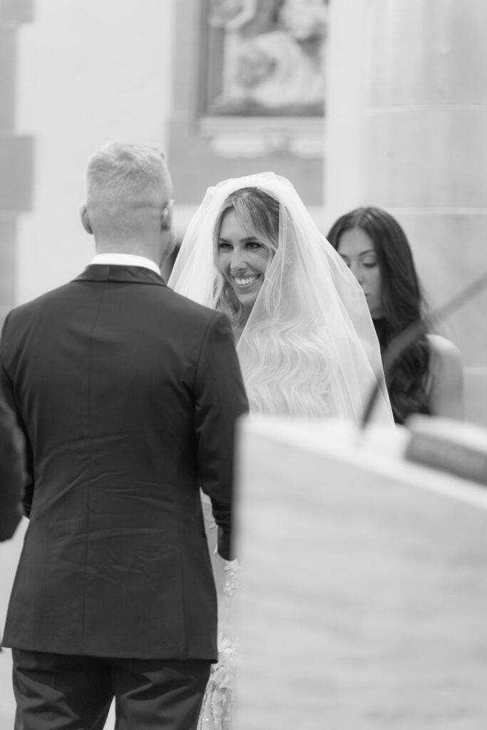 The groom stands with his back to the viewer while facing his bride, who is smiling at a Russos on the Bay Wedding.