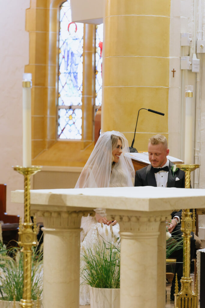 A bride and groom sitting together during their Catholic wedding ceremony at Russos on the Bay.