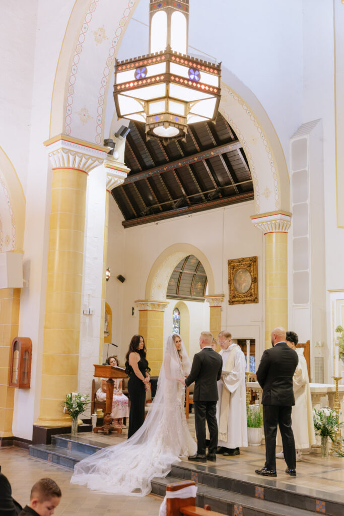 A couple standing at the altar with a priest during their Catholic wedding ceremony at Russos on the Bay.