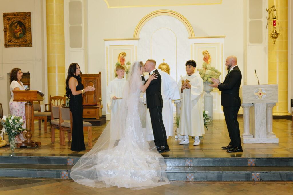 A newlywed couple shares a kiss at a Catholic ceremony as part of their Russos on the Bay wedding.