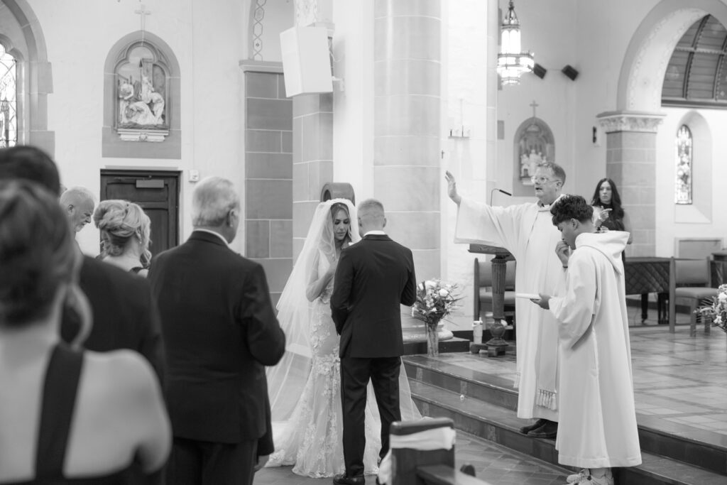 A bride and groom stand before a priest during their Catholic wedding ceremony at Russos on the Bay.