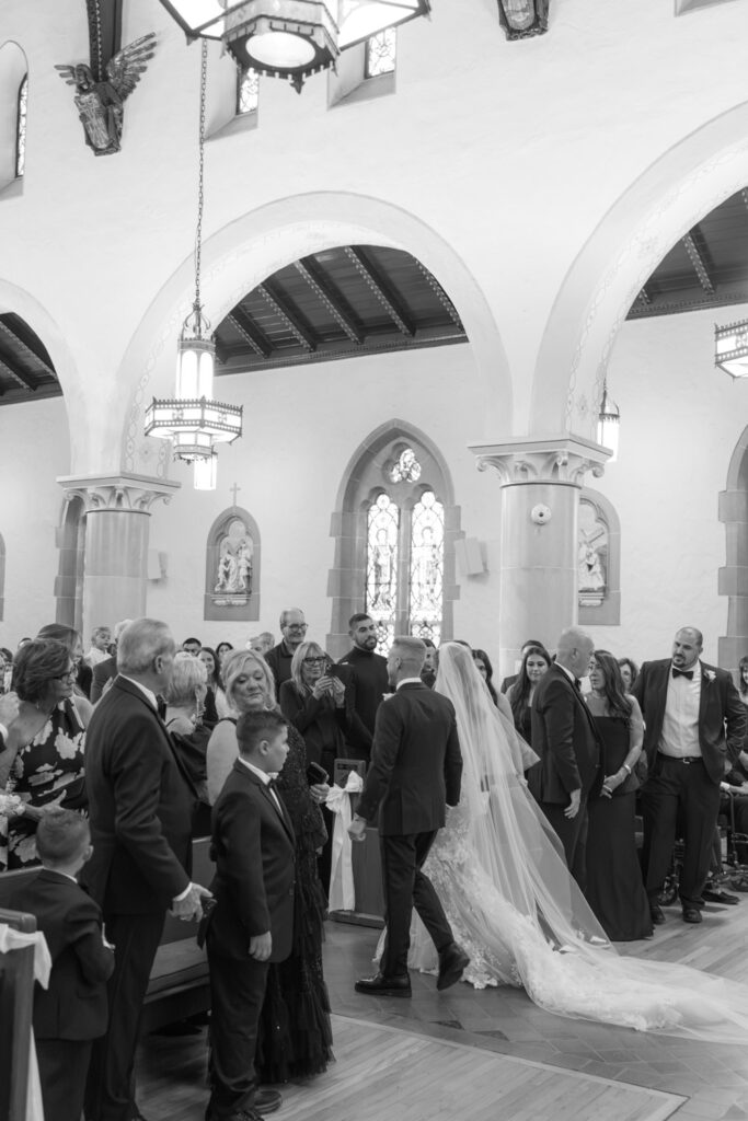 A groom leads his bride down the aisle of a Catholic church during a Russos on the Bay wedding.